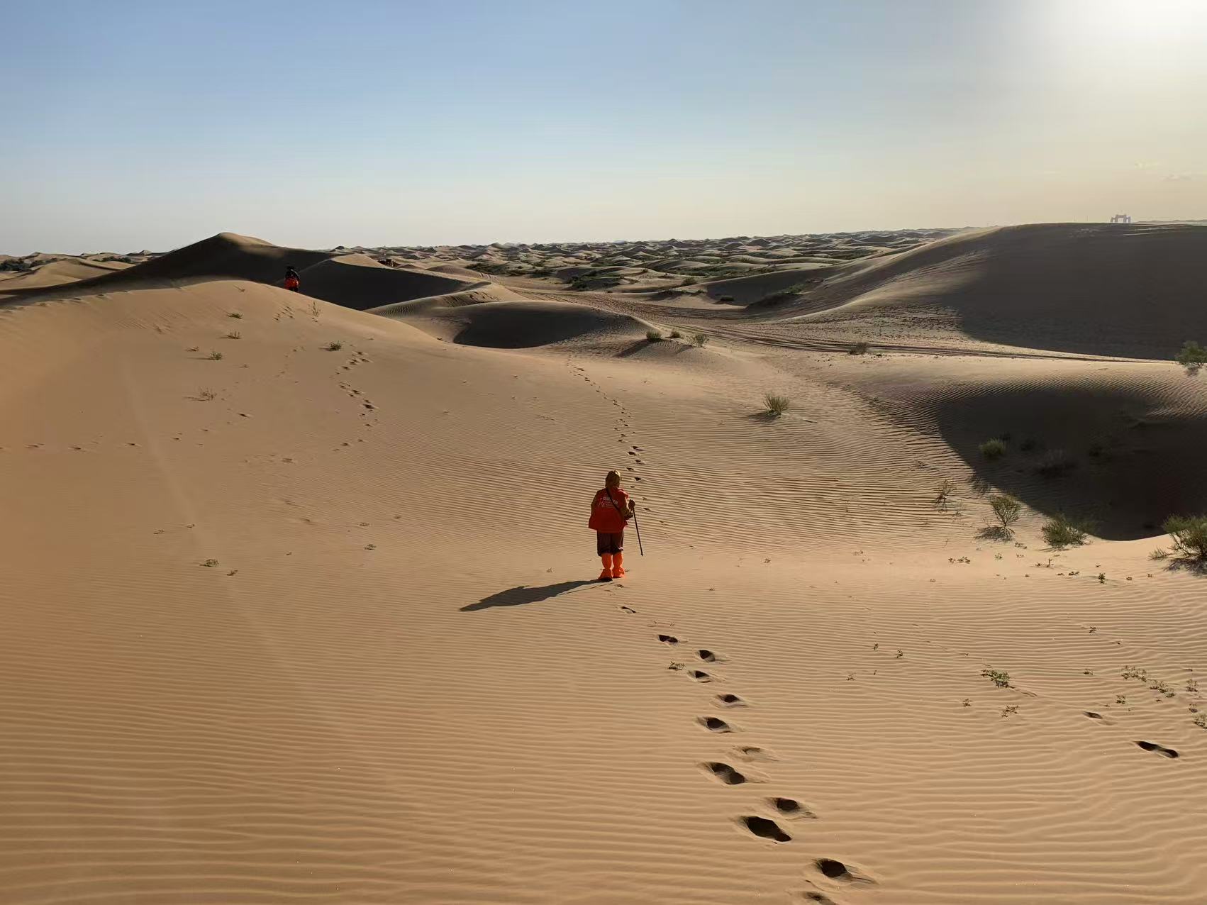Sunlit sand dunes, with footprints leading toward a distant walker.